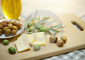 Green olives with cheese and olive branch on a wooden board