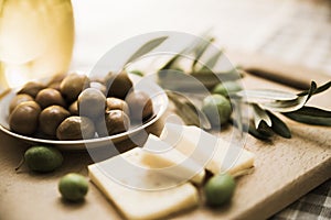 Green olives with cheese and olive branch on a wooden board