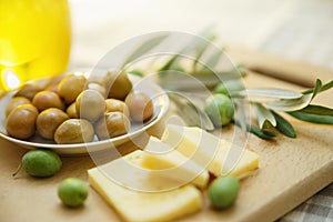 Green olives with cheese and olive branch on a wooden board
