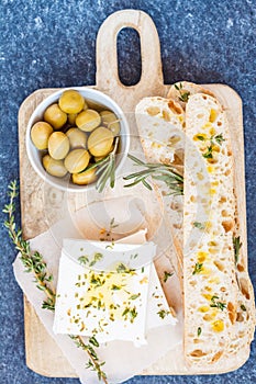 Green olives, feta cheese and fresh ciabata on a wooden board