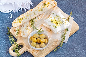 Green olives, feta cheese and fresh ciabata on a wooden board