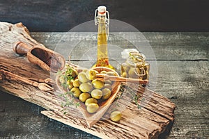 Green olives in a heart-shaped wooden bowl on a wooden background, a bottle of olive oil with olives in solution and a glass jar.