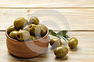 Green olives with leaves in a wooden bowl with olive oil on a natural wooden table. close-up