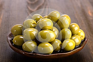 Green olives in oil stacked on a ceramic plate