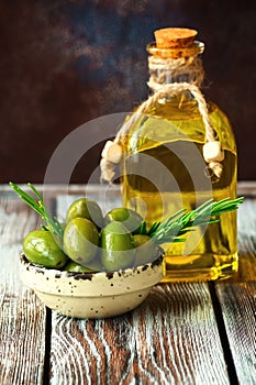 Green olives, olive oil in a bottle and a fresh sprig of rosemary on a wooden table. Rustic style. Selective focus