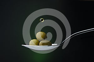 Green olives on a spoon on a dark background, a drop of olive oil