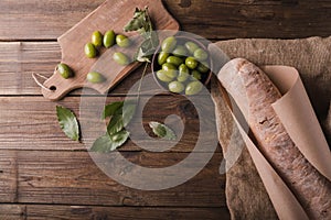 Green olives on a wooden board ciabatta, bay leaf on wooden background