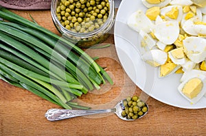 Green onions, chopped eggs on a plate and canned peas on a wooden board. The concept of cooking spring salad.