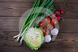 Green onions, yellow peppers, cherry tomatoes, slot and cabbage on dark wooden table. Top views, close-up