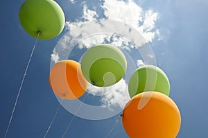 Green and orange balloons flying towards the sun