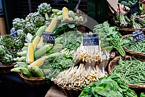 Green organic vegetables in display for sale at a street food market, with names displayed in English, globe artichokes, white asp