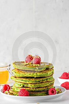 Green pancakes with matcha tea, raspberries, pistachios and honey. healthy breakfast. vertical orientation