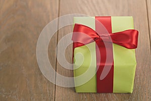 Green paper gift box with red ribbon bow on oak table