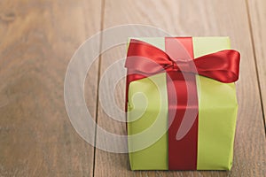 Green paper gift box with red ribbon bow on oak table