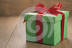 Green paper gift box with red ribbon bow on oak table