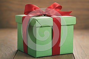 Green paper gift box with red ribbon bow on oak table