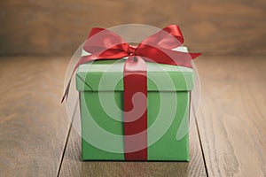 Green paper gift box with red ribbon bow on oak table