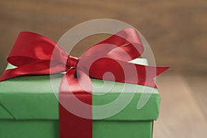 Green paper gift box with red ribbon bow on oak table