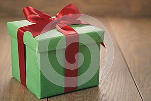 Green paper gift box with red ribbon bow on oak table