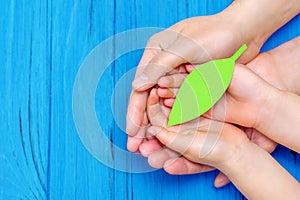 Green paper leaf in hands of adult and child