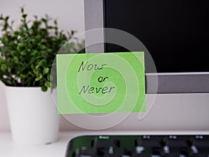 A green paper notes with the reminder Now or Never on it sticked on to monitor at an office workplace