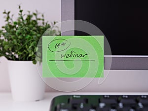 Green paper notes with the reminder 19-00 Webinar on it sticked on to a monitor at an office workplace