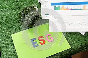 Green paper with the word ESG written on it. The paper is green and has a graph on it. The graph shows three lines, one for each