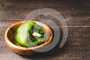 Green paprika on a wooden bowl /Green paprika pepper on a wooden bowl over dark background. Selective focus