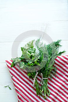 Green parsley and dill leaves on natural linen napkin on wooden background