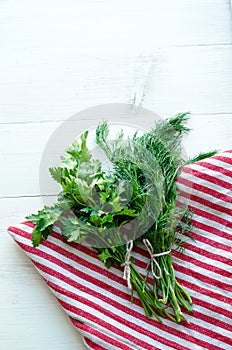 Green parsley and dill leaves on natural linen napkin on wooden background