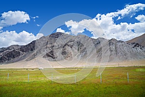 Green pasture with yurt at the foot of barren rocky mountains