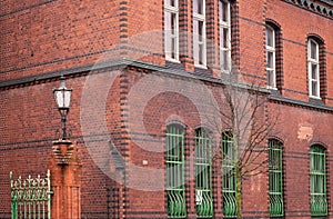 Green patina copper fence in front of old green orange red brick wall of an old building corner and huge windows. Architecture