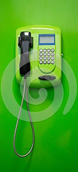Green payphone with a black tube and blue display