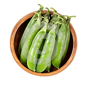 Fresh pea pods, containing green peas, in a wooden bowl