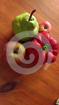 Green pear, two red apples and red sweet pepper on wooden table