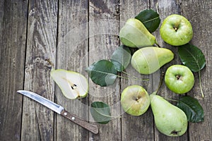 Green pears , apples and knife with leafs on old, wooden table.