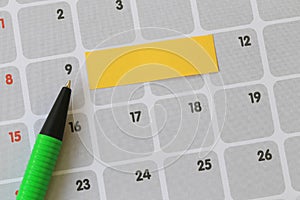 Green pen points to a nine number of calendar and have blank yellow note paper.