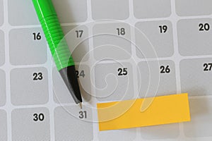 Green pen points to a thirty one number of calendar and have blank yellow note paper.