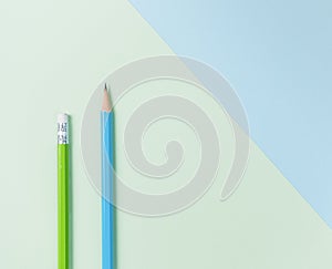 Green pencil and blue pencil on green and light blue background.