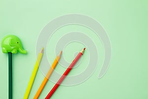 Green pencil sharpener and five pencils on a pale green background