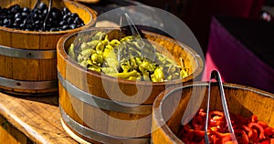 Green pepperone, black olives and sliced red peppers in large wooden vats photo