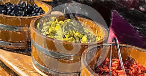 Green pepperone, black olives and sliced red peppers in large wooden vats photo