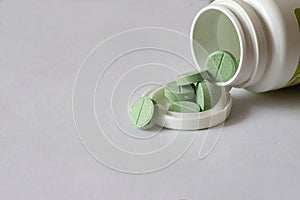 Green phyto pills poured from a bottle on a white background.