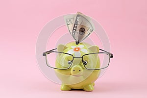 Green piggy bank with glasses and money on a bright pink background. Finance, savings, money