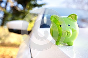 Green piggy bank money box on top of car hood, new vehicle purchase, insurance or driving and motoring cost