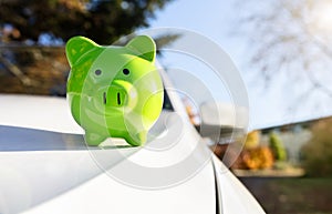 Green piggy bank money box on top of car hood, new vehicle purchase, insurance or driving and motoring cost