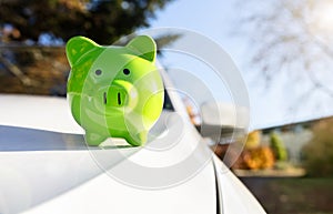 Green piggy bank money box on top of car hood, new vehicle purchase, insurance or driving and motoring cost photo