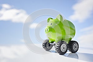Green piggy bank money box on wheels against blue sky background, new vehicle purchase, insurance or driving and motoring cost photo