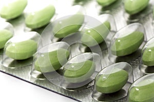 Green pills in a blister pack, closeup with selected focus