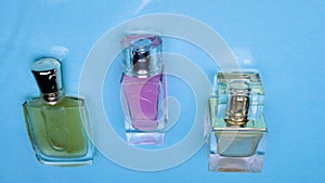 A green, pink and blue perfume bottle lies in the waves of water on a blue background